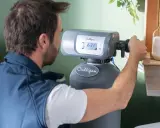 Un homme ajuste le panneau de contrôle d'un symbole adoucisseur d'eau Culligan. Des serviettes sont empilées à gauche.