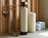 Système d'adoucisseur d'eau avec réservoir de sel, tuyauterie en cuivre et sacs de sel pour une eau plus douce.