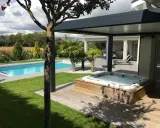 Un spa bouillonnant sur une terrasse en bois, à côté d'une piscine bleue. Le tableau temps de filtration piscine est visible dans le jardin luxuriant.
