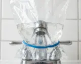 Un sac en plastique rempli d'eau est attaché à un robinet avec un élastique bleu. Une méthode pour enlever le calcaire de l'eau naturellement.