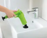 Main verte, un pistolet déboucheur est utilisé pour dégager un lavabo blanc.