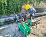 Un ouvrier utilise une machine de soudure pour joindre un gros tuyau noir. L'équipement comprend une douille à souder et une unité de contrôle verte.