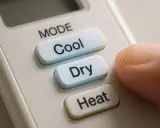 Doigt appuyant sur le bouton "Cool" d'une télécommande clim, offrant le choix entre clim heat ou cool.