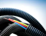 Trois fils électriques colorés sortent d'un tube plastique souple noir et ondulé, prêt à protéger les câbles.