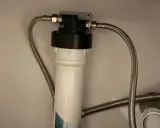 Système de filtration d'eau sous évier avec un cartouche charbon actif blanc et noir, relié par des tuyaux flexibles.