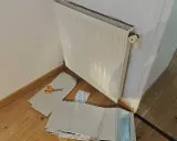 Un radiateur derrière une porte, prêt à être isolé avec des feuilles argentées et des ciseaux.