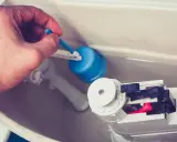 Main d'homme ajustant le flotteur bleu d'une chasse d'eau qui ne se remplit pas pour un wc suspendu.