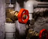 Gros plan sur un joint d'électrovanne avec une poignée rouge vif, faisant partie d'un système de plomberie complexe.