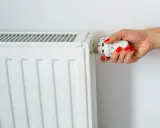 Main d'une femme aux ongles rouges tournant le thermostat pour savoir comment éteindre un radiateur électrique.