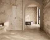 Douche moderne avec robinetterie dorée sur un sol de salle de bain en travertin. L'espace invite à la détente.