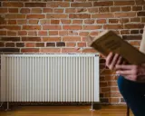 Un homme lit un livre près d'un radiateur blanc. La question quelle puissance de radiateur pour 25 m2 est au cœur de ce décor cosy.