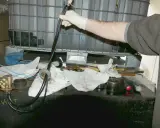 Main d'une personne en gant blanc manipulant un tube avec des fils bleus, près d'une cuve à fioul et d'une crépine.