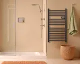 Salle de bain moderne avec douche, porte-serviettes chauffant noir et panier en liège. Le disjoncteur du sèche serviette est visible.