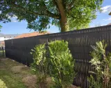 Clôture ajourée noire, offrant une protection discrète pour les tuyaux PVC. Des arbustes verts bordent cette barrière moderne.