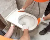 Mains gantées installent un WC suspendu. L'opération est délicate, mais le résultat sera moderne et pratique.
