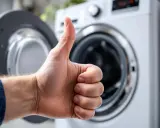 Pouce levé devant une machine à laver ouverte, signe d'un branchement machine à laver réussi.