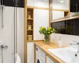 Une petite salle de bain moderne avec une douche, un lavabo, une machine à laver et des paniers en osier sur des étagères en bois.
