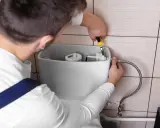 Un plombier répare une chasse d'eau qui coule. Il utilise une pince pour ajuster le mécanisme interne du réservoir.