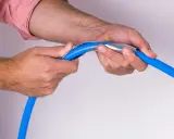 Mains bleues tenant un tuyau bleu avec un outil métallique pour former un coude boule.