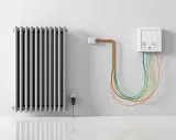 Radiateur argenté avec un branchement radiateur électrique coloré. Un boîtier mural blanc avec prises et câbles arc-en-ciel.