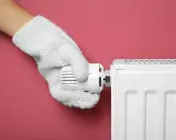 Main tenant, avec un gant blanc, ajuste le thermostat d'un radiateur pour choisir entre le chauffage mode eco ou confort.