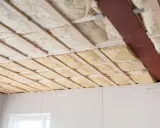 Isolation thermique plafond en cours d'installation, avec des panneaux de laine minérale entre les solives en bois.
