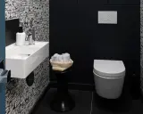 Une salle de bain moderne avec un papier peint original, un petit lavabo blanc, des serviettes roulées et une cuvette suspendue. La deco wc est soignée.