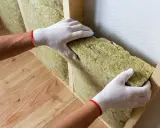 Mains gantées insèrent un isolant dans une structure en bois pour isoler sa maison.