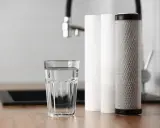 Verre d'eau pure à côté de cartouches filtrantes. Une solution pour la dureté de l'eau à Rouen.
