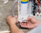 Mains d'un technicien connectant un tuyau à un système de filtration d'eau, peut-être pour résoudre un problème où le sel de mon adoucisseur ne fond pas.