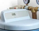 Adoucisseur d'eau moderne avec écran digital affichant l'heure. Les tuyaux et manomètres suggèrent une installation de rupture de charge adoucisseur.