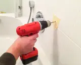 Main tenant perce le carrelage de la salle de bain pour installer un accessoire.