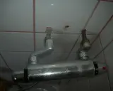 Un excentrique robinet de douche, fixé au mur carrelé, avec des tuyaux argentés et des indications de température.