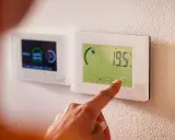 Main d'une personne ajustant un thermostat intelligent, symbole de la domotique sans fil. Confort et efficacité énergétique à portée de main.