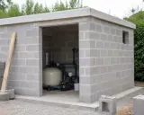 Construction d'un local technique pour piscine en dur. L'abri en parpaings abrite le système de filtration.