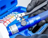 Main bleue avec un outil de sertissage. Le kit contient des cosses colorées.