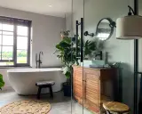 Une salle de bain moderne et épurée, parfaite pour refaire salle de bain. Baignoire îlot, meuble en bois, plantes vertes et lumière naturelle.