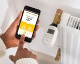 Maintenant, contrôlez votre chauffage à distance avec des solutions domotiques. Une main utilise un smartphone pour régler la température d'un radiateur.