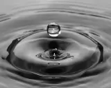Goutte d'eau en suspension au-dessus de son impact, créant des ondulations. L'eau calcaire reflète la lumière.