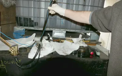 Main d'une personne en gant blanc manipulant un tube avec des fils bleus, près d'une cuve à fioul et d'une crépine.