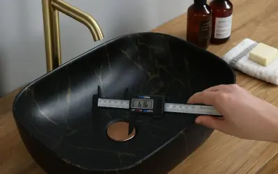 Mesure du diamètre de la bonde universelle d'un lavabo noir marbré d'or.