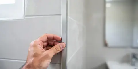 Main tenant vérifie le joint en L d'un profilé de finition sur un mur carrelé.