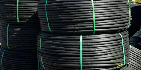 Rouleaux de tube plastique flexible noir, attachés par des sangles vertes, prêts pour l'irrigation.