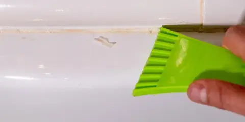 Outil vert raclant du mastic durci sur une surface blanche.