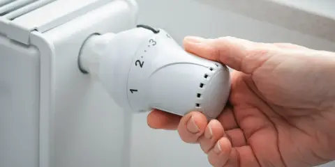 Main tenant ajuste le thermostat d'un radiateur, se demandant s'il faut fermer les radiateurs en été pour économiser de l'énergie.