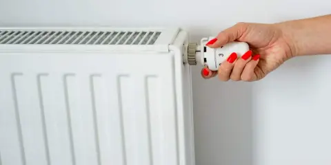 Main d'une femme aux ongles rouges tournant le thermostat pour savoir comment éteindre un radiateur électrique.