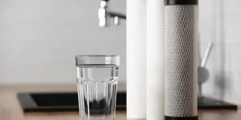 Verre d'eau pure à côté de cartouches filtrantes. Une solution pour la dureté de l'eau à Rouen.