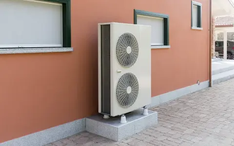 Unité extérieure de pompe à chaleur, avec ses deux ventilateurs, installée sur un socle devant un mur ocre. Le poids de cet appareil assure sa stabilité.