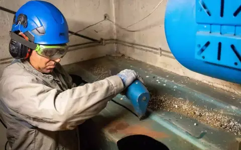 Un ouvrier en casque bleu et lunettes effectue l'inertage d'une cuve, utilisant un outil pour nettoyer la surface.