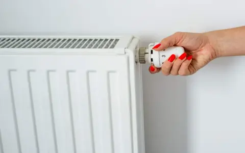 Main d'une femme aux ongles rouges tournant le thermostat pour savoir comment éteindre un radiateur électrique.